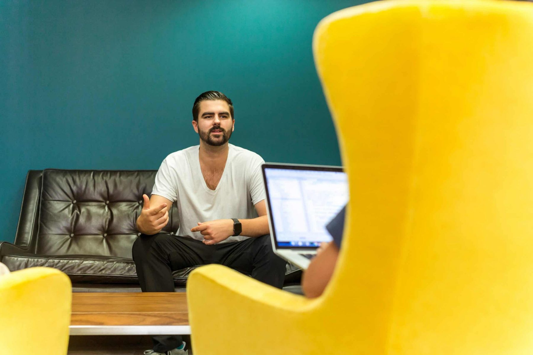 man interviewing in front of person in yellow chair with laptop